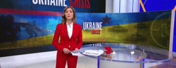 A news anchor standing in front of a 'Ukraine Crisis' graphic